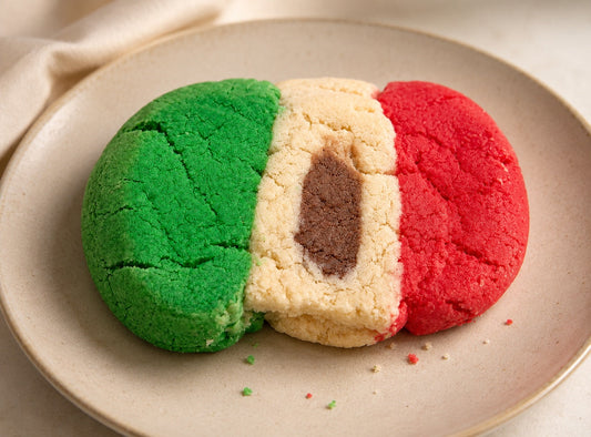 A Mexican concha decorated in the colors of the Mexican flag, with green, white, and red sugar topping and a chocolate center, photographed on a ceramic plate.