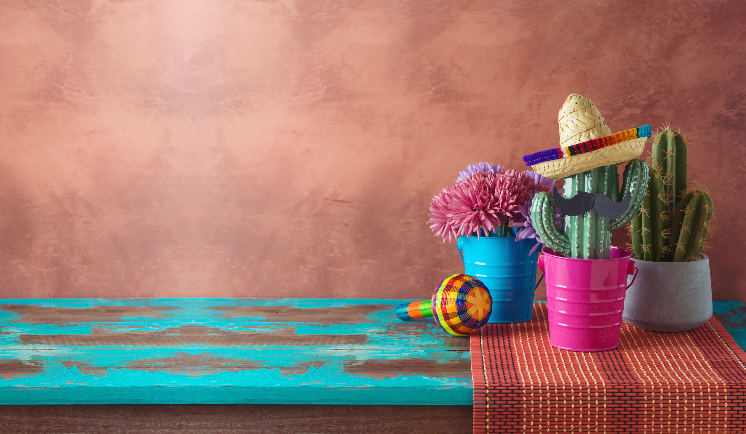 Decorative items including cacti, sombrero, maracas, and colorful buckets on a textured surface with a brown background. casa de queta.